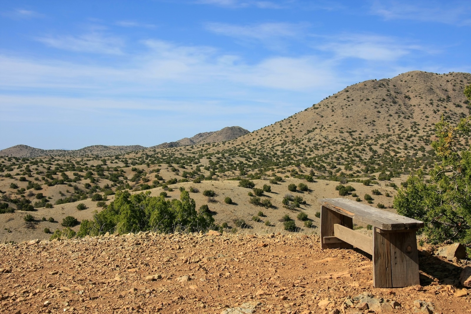 A wooden bench on a summit in Cerillos Hills State Park with surrounding mountains.